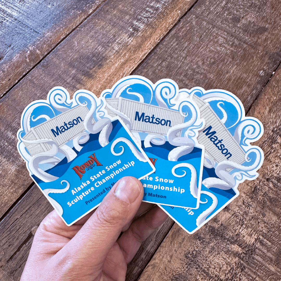 Hand holding a batch of kraken stickers promoting the Alaska State Snow Sculpture Championship.